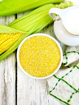 Corn grits in a bowl, cobs, a jug of milk and a napkin on the background light wooden boards on top