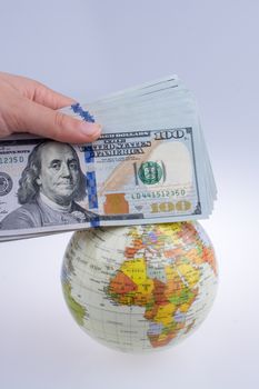 Human hand holding American dollar banknotes by the side of a model globe on white background