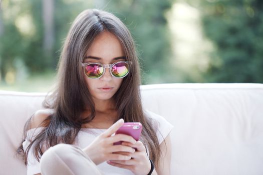 Beautiful young girl with smartphone sitting outdoors