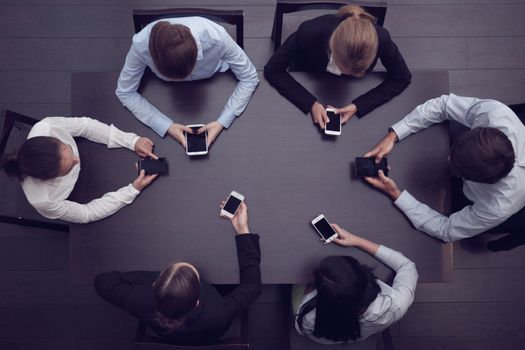 Business people with smartphones sitting around the table, top view