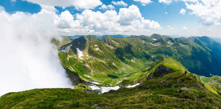 mountainous panorama with rising clouds. beautiful landscape with some snow on grassy hillsides. popular destination for hiking in Fagaras mountains of Romania