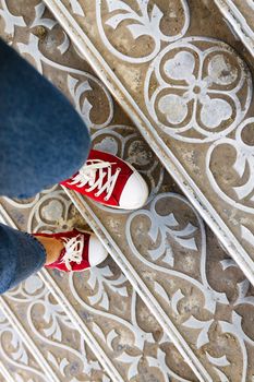 legs in jeans and red sneakers on an antique metal staircase. Top view