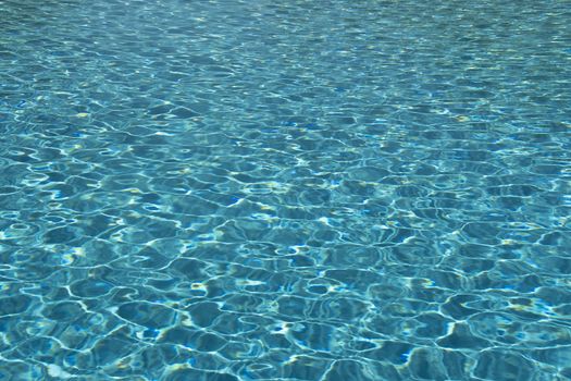 Clear blue water in the swimming pool on a sunny day with ripples on the surface