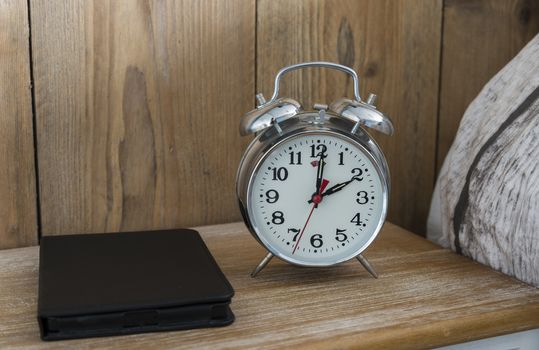 An old fashioned silver coloured bed side analogue pre digital alarm clock and modern ereader on bedside table