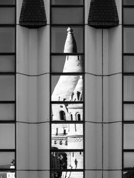 Detailed view of warped reflection of Fisherman's Bastion, aka Halaszbastya, fairy tale towers in windows of modern hotel. Architectural constrast of historical landmark and hated modern architecture of communistic Hungary. Budapest, capital city of Hungary, Europe. UNESCO World Heritage Site. Black and white image.