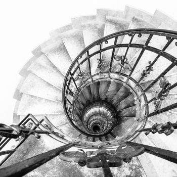 Upside view of indoor spiral winding staircase with black metal ornamental handrail. Architectural detail in St. Stephen's Basilica in Budapest, Hungary. Black and white image.