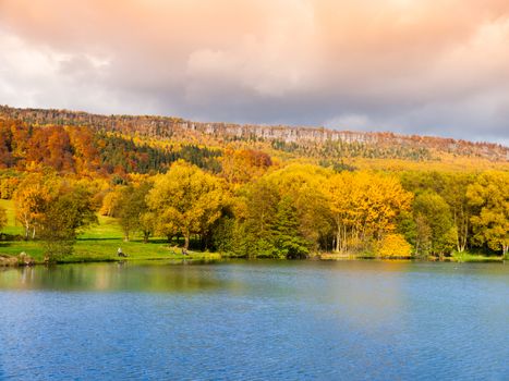 Sandstone rock formation in the middle of colorful autumn forest. Water surface on the foreground. Dramatic evening view. Tisa Rocks, aka Tiske Walls, Czech-Saxon Switzerland, Czech Republic