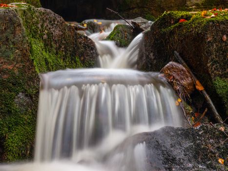 Autumnal mood in the forest with small creek waterfalls. Long exposure shot with blurred silky water stream.