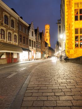 Bruges by night. Cobbled street and illuminated historical city centre with Belfort Tower, Belgium, Europe.