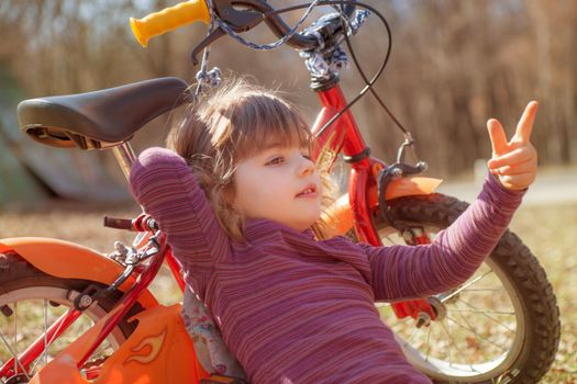A young girl around four is leaning on a bike pointing forward.