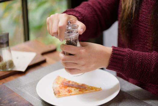 Woman hands using black pepper and salt shaker on the slices of pizza
