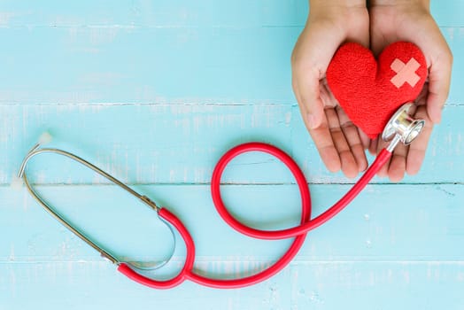 World health day, Healthcare and medical concept. Woman hand holding red heart with Stethoscope, notepad or notebook, thermometer and yellow Pill on Pastel white and blue wooden table background texture.