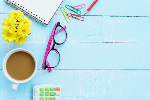 Top view office table with workspace and office accessories including calculator, mouse, keyboard, glasses, clips, flower, pen, pencil , note book and laptop on bright green wooden background.