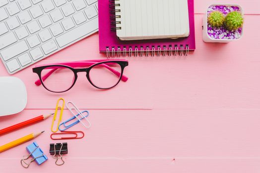 Top view office table with workspace and office accessories including calculator, mouse, keyboard, glasses, clips, flower, pen, pencil, note book, laptop and coffee on pink wooden background.