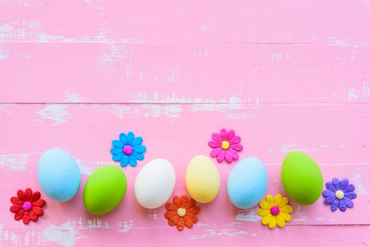 Row Easter eggs with colorful paper flowers on bright pink and white wooden background.