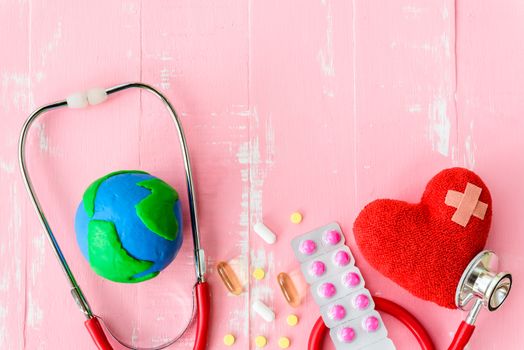 World health day, Healthcare and medical concept. Red heart with Stethoscope, handmade globe, thermometer and yellow Pill on Pastel white and pink wooden background.