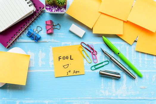 April fool's day celebration concept. office table with office accessories laptop, keyboard, mouse covered in sticky notes  on blue wooden background.