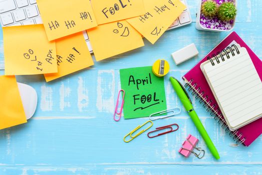 April fool's day celebration concept. office table with office accessories laptop, keyboard, mouse covered in sticky notes  on blue wooden background.