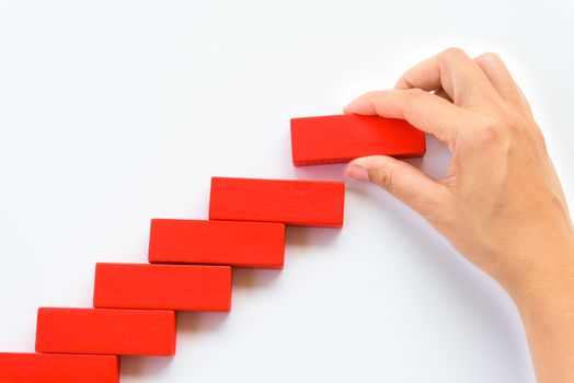 Concept of building success foundation. Women hand put red wooden block on yellow wooden blocks in the shape of a staircase