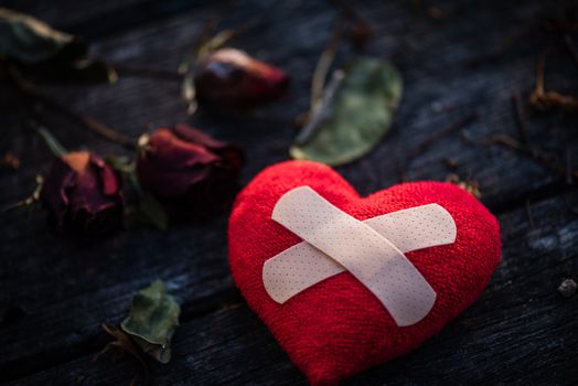 First Aid Band Cushioned Plaster Strip Medical Patch glued on red heart with dried red rose on wooden background. Heart broken, Love and Valentines day concept.