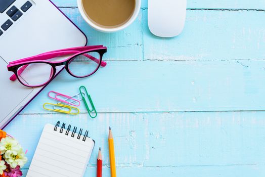 Top view office table with workspace and office accessories including calculator, mouse, keyboard, glasses, clips, flower, pen, pencil, Pencil sharpener , note book, laptop and coffee on bright green wooden background.