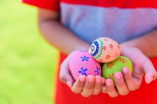 Happy easter! Close up of little kid holding colorful Easter eggs on green grass field background.