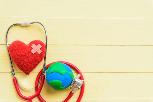 World health day, Healthcare and medical concept.  Stethoscope with handmade globe and Red heart on Pastel white and yellow wooden background.