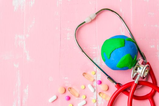 World health day, Healthcare and medical concept. Red heart with Stethoscope, handmade globe, thermometer and yellow Pill on Pastel white and pink wooden background.