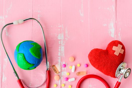 World health day, Healthcare and medical concept. Red heart with Stethoscope, handmade globe, thermometer and yellow Pill on Pastel white and pink wooden background.