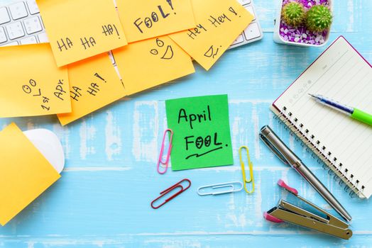 April fool's day celebration concept. office table with office accessories laptop, keyboard, mouse covered in sticky notes  on blue wooden background.