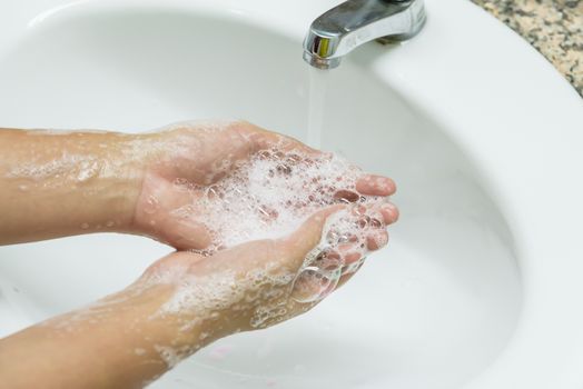 Selective focus of woman washing hands with soap under the faucet with water  in the bathroom.