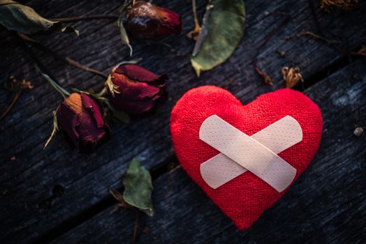 First Aid Band Cushioned Plaster Strip Medical Patch glued on red heart with dried red rose on wooden background. Heart broken, Love and Valentines day concept.