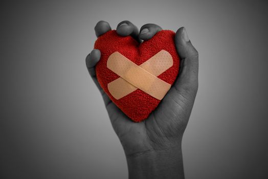 Close up Young woman hand holding red heart glued by Cushioned Plaster Strip Medical Patch on wooden background. Heart broken, Love and Valentines day concept.