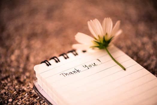 Thank You text on a white page note book with romantic white flower on wooden background.