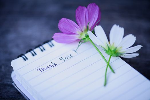 Thank You text on a white page note book with romantic white flower on wooden background.