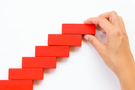 Concept of building success foundation. Women hand put red wooden block on yellow wooden blocks in the shape of a staircase