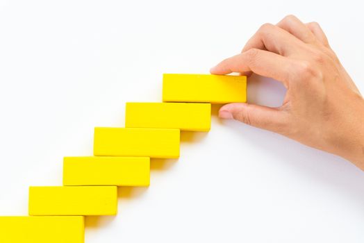 Concept of building success foundation. Women hand put red wooden block on yellow wooden blocks in the shape of a staircase