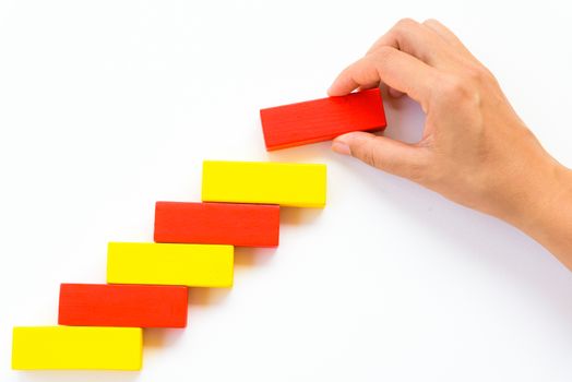 Concept of building success foundation. Women hand put red wooden block on yellow wooden blocks in the shape of a staircase