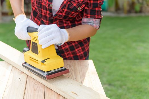 Womam Carpenter working with wood electrical sanding machine