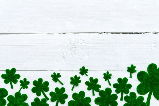 Happy St Patricks Day message and a lot of green paper clover leaf on white wooden background