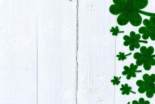 Happy St Patricks Day message and a lot of green paper clover leaf on white wooden background