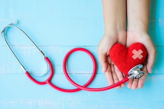 World health day, Healthcare and medical concept. Woman hand holding red heart with Stethoscope, notepad or notebook, thermometer and yellow Pill on Pastel white and blue wooden table background texture.