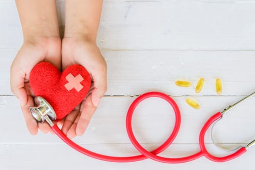 World health day, Healthcare and medical concept. Woman hand holding red heart with Stethoscope, notepad or notebook, thermometer and yellow Pill on Pastel white and blue wooden table background texture.