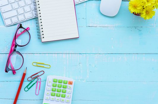 Top view office table with workspace and office accessories including calculator, mouse, keyboard, glasses, clips, flower, pen, pencil , note book and laptop on bright green wooden background.