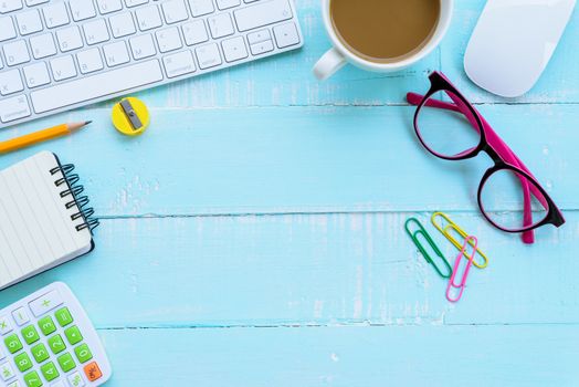 Top view office table with workspace and office accessories including calculator, mouse, keyboard, glasses, clips, flower, pen, pencil, Pencil sharpener , note book, laptop and coffee on bright green wooden background.