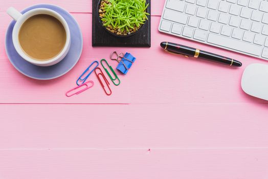 Top view office table with workspace and office accessories including calculator, mouse, keyboard, glasses, clips, flower, pen, pencil, note book, laptop and coffee on pink wooden background.