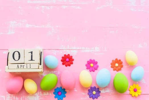 Wooden block calendar for Easter Day, April 1. Row Easter eggs with colorful paper flowers and red ribbon on bright pink and white wooden background.