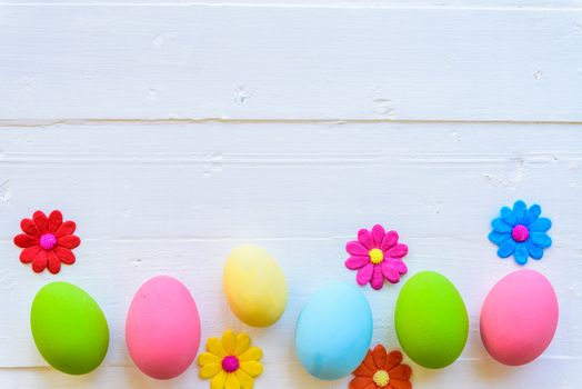 Row Easter eggs with colorful paper flowers on bright pink and white wooden background.