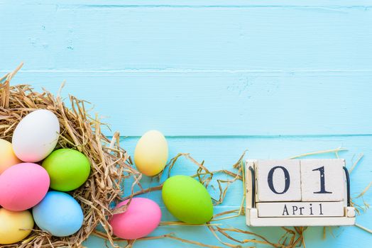 Wooden block calendar for Easter Day, April 1. Colorful of Easter eggs in nest on pastel color bright blue and white wooden background.