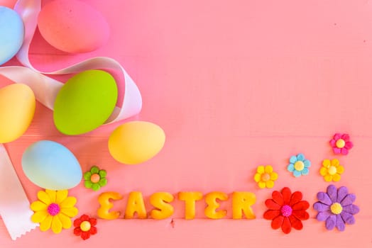 Easter eggs with colorful paper flowers and alphabet cracker in Easter text on bright pink wooden background.